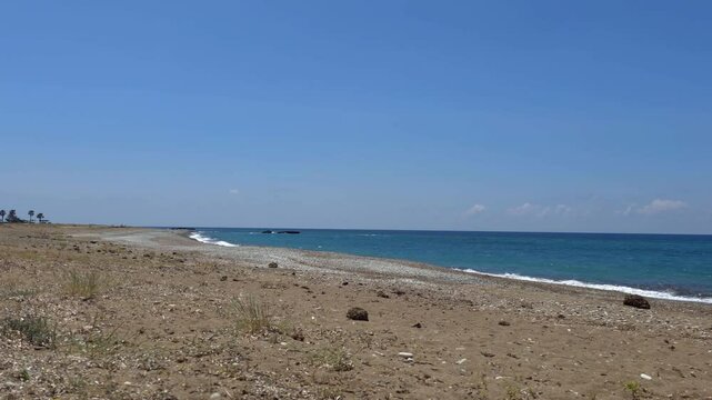 Crystal-clear 4K view of Mandria Beach in Cyprus with pebbles, gentle sea waves, and blue sky. A peaceful coastal moment&mdash;ideal for travel, nature, and relaxation footage in ultra HD.