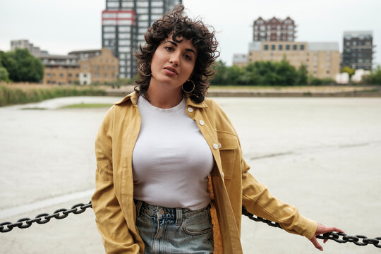 Young woman posing by a chain fence in an urban setting