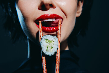 Woman with red lips holding sushi with chopsticks, showcasing vibrant colors and an artistic...