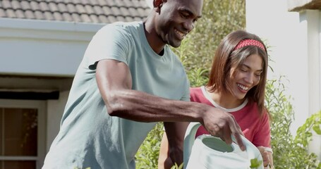 diverse couple watering plants in garden, enjoying sunny day - Powered by Adobe