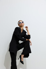 fashion woman wearing black outfit and white sunglasses poses confidently against white background,...