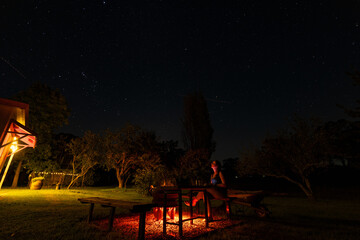 Woman sitting by backyard fire pit looking up at the stars in the night sky above