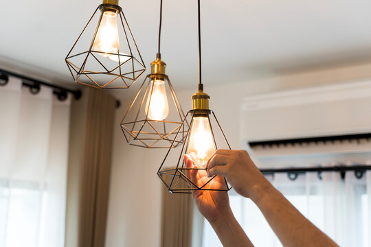 Hand changing light bulb in modern pendant lamp with geometric metal frame, energy saving home interior concept