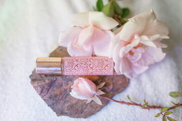 Decorated pink essential oil roller bottle with fresh roses and diffuser