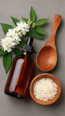 Brown glass dropper bottle, rice, wooden spoon, white flower, and green leaves on gray background