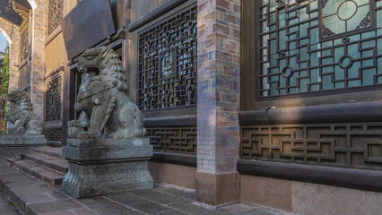 Obraz premium Stone sculptures of stylized lions are installed on pedestals at the entrance to the building. Carved ornaments. Bars on the windows. China.