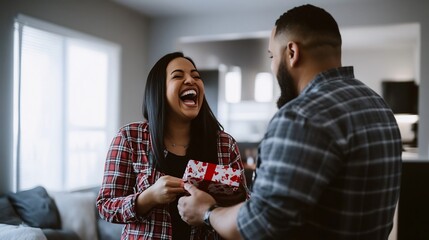 Woman laughing receiving a gift from a man in a plaid shirt in a living room with natural light source