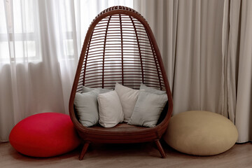Cozy reading nook with a stylish rattan egg chair, soft cushions, and colorful floor poufs by a window with flowing curtains