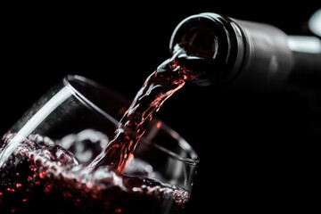 Red wine pouring from an unbranded bottle into a glass on a dark background