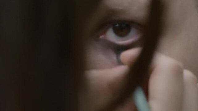 Close-up: Professional makeup artist applying dark, dramatic eye makeup on model for Halloween inspired gothic beauty look, creating intense, spooky transformation