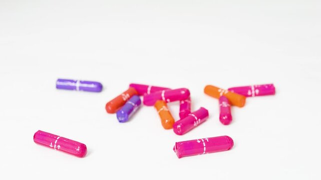 Feminine hygiene tampons tumbling, softly bouncing across white surface, displaying dynamic motion with vibrant pink, orange, purple colors
