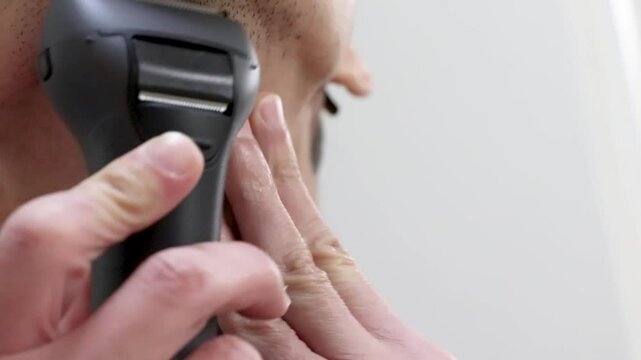 電気シェーバーで顎のひげを剃る男性