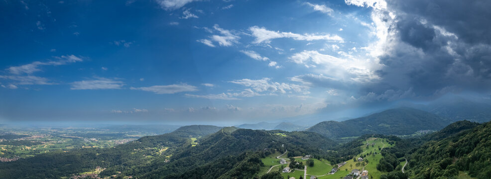 Drone panorama of the Ivrea Morainic Amphitheatre seen from Brosso, Val Chiusella, Italy, showing lush green plains, woods, and scattered villages under clear sky, high drone shot, slow motion