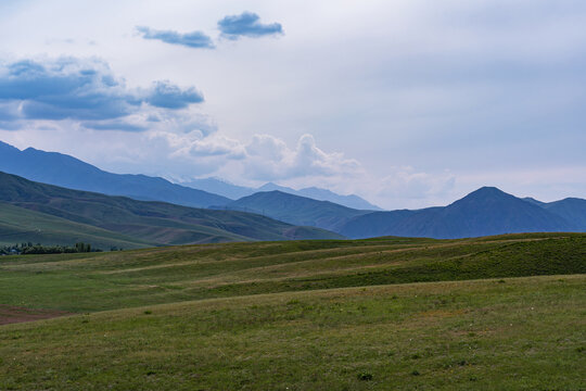 A mountainous summer landscape with views of green and yellow hills, high snow-capped mountains and a blue sky with clouds.