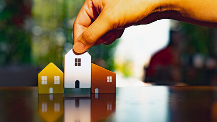 Hand choosing mini wood house model from model and row of coin money on wood table, selective...