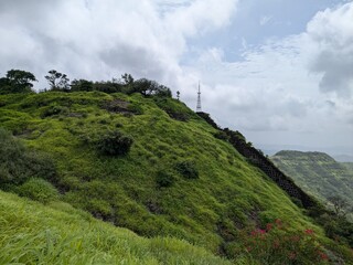 Lush green hillside with communication towers under dramatic cloudy sky