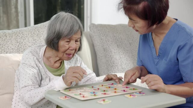 Nurse in nursing home helping a senior woman with number puzzle game. Dementia, Alzheimer's disease.