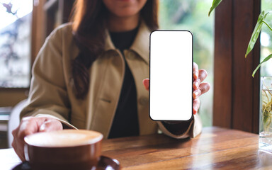 Mockup image of a woman holding and showing mobile phone with blank white screen in cafe