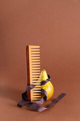 Wooden comb with wide teeth and pear at brown background, contemporary still life composition for modern editorial magazine , Conceptual photo