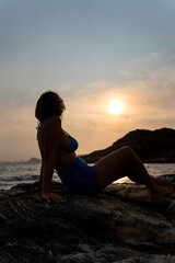 Young woman watching sunset on a rock at the beach