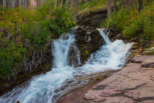 Serene waterfall cascades over rocky terrain in a lush forest during a sunny afternoon