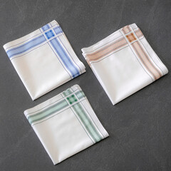 Set of folded handkerchiefs with a striped design is placed on a dark stone surface.