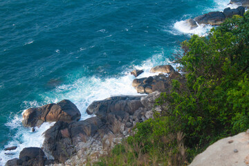 Scenic tropical coastline with steep rocky cliffs and lush green forest descending into turquoise...