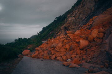 Landslide blocking a rural mountain road with scattered orange rocks and debris. Natural disaster...