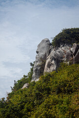 A natural rock formation resembling a human profile rises above the forested hillside on Cham...