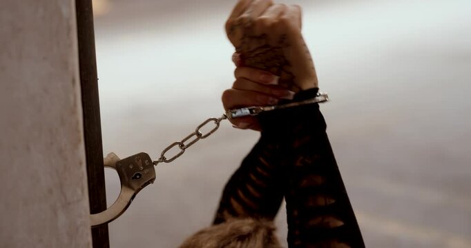 Tattooed woman handcuffed to a pillar in industrial warehouse struggling to escape, close up handcuffed