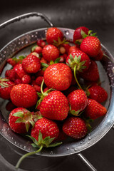 A close-up view of fresh red strawberries with green stems inside a wet metal colander.