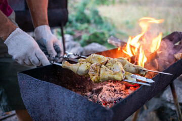 Grilling marinated chicken skewers over an open flame in a rustic outdoor setting