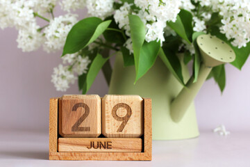 Wooden perpetual calendar showing june 29th with white lilac flowers in watering can