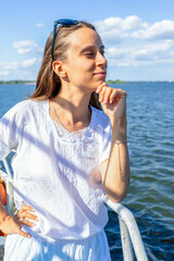 Young woman in white shirt enjoying a sunny day by the water with a thoughtful expression