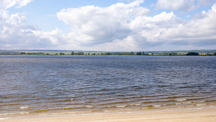 Serene landscape with calm water, sandy beach, and dramatic clouds in a tranquil setting
