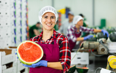 Happy Hispanic woman fruit processing factory worker holding half of ripe red watermelon while...