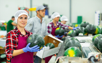 Cheerful Hispanic woman working on industrial sorting line in fruit warehouse, preparing...