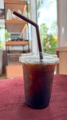 Iced Americano in takeaway plastic glass with brown straw