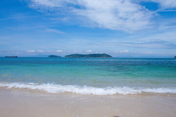Tropical beach with soft sand and emerald water surrounded by lush green hills, captured in Cham...