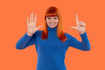 Young woman with vibrant red hair happily showing seven 7 number fingers against an orange...