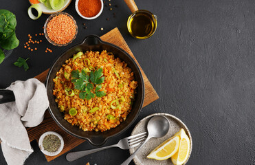Vegetarian dish of red lentil leek and carrot in the black pan on black background with ingredients, top view, copy space