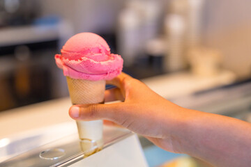 Hand holding delicious pink ice cream cone in gelateria display case