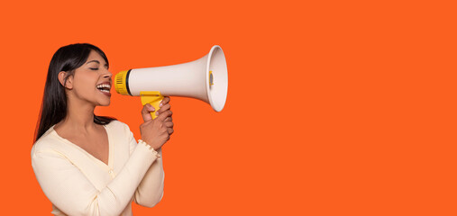 Young woman enthusiastically using a megaphone to express ideas against a bright orange background