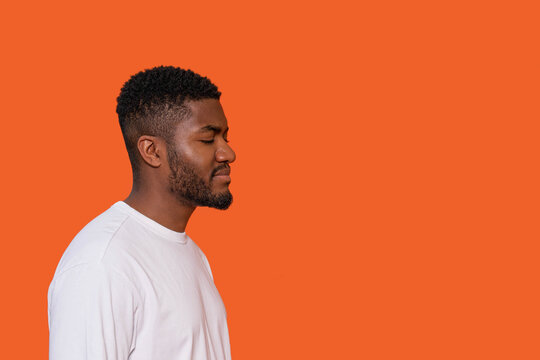 Young man with short curly hair stands against an orange background with eyes closed and a calm expression reflecting a moment of introspection