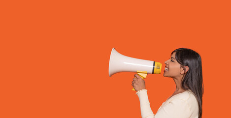 Young woman passionately advocates using a megaphone against a vibrant orange background with enthusiasm and energy