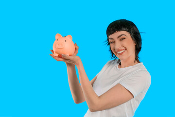 Cheerful woman holding a piggy bank against a bright blue background while promoting savings in a...