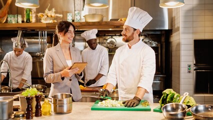 Portrait of attractive professional caucasian chef chopping vegetables and talking with beautiful...