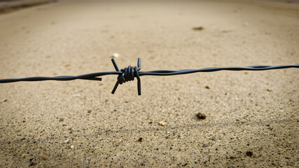 Close-up of barbed wire stretched across a concrete floor, symbolizing safety, boundary, danger and restriction.