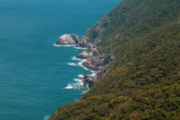 Scenic tropical coastline with steep rocky cliffs and lush green forest descending into turquoise...