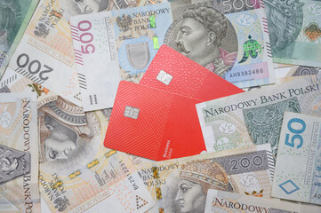 Two red bank cards lie on Polish zloty notes, illustrating the contrast between digital and cash payments. Perfect for financial themes, online banking, and economic transitions.